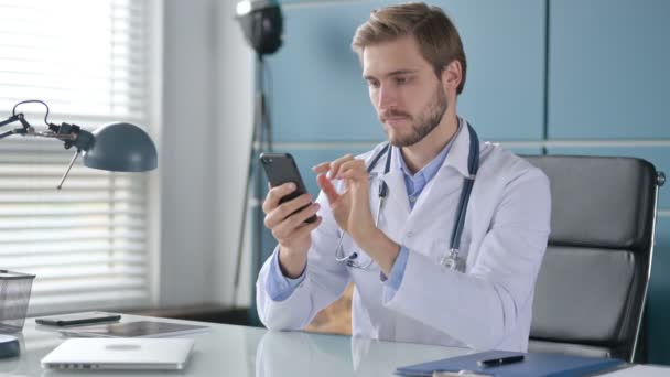 Γιατρός που χρησιμοποιεί Smartphone ενώ κάθεται στην κλινική — Αρχείο Βίντεο