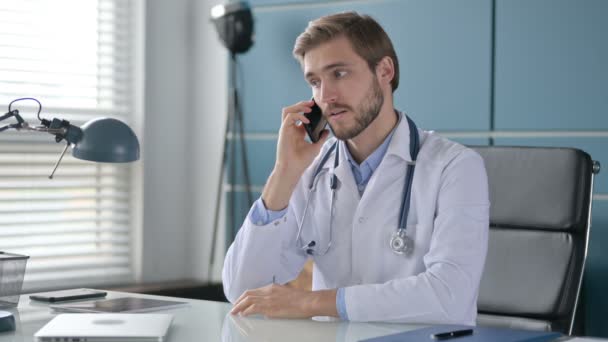 Lekarz rozmawiający na smartfonie podczas siedzenia w klinice — Wideo stockowe
