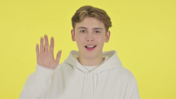 Homem jovem acenando, dando boas-vindas no fundo amarelo — Vídeo de Stock