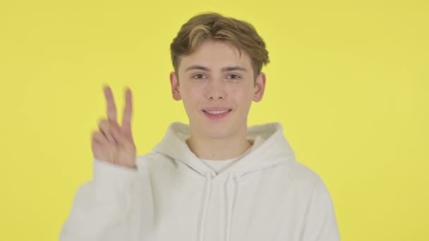 Молодой человек показывает знак победы на жёлтом фоне — стоковое видео
