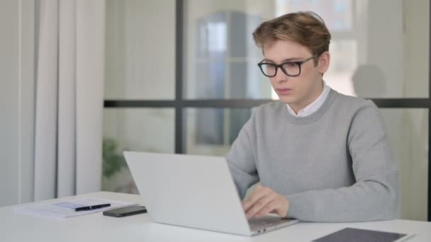 Ung man tittar på kameran när du använder laptop i moderna kontor — Stockvideo