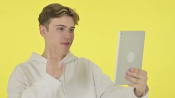 Видеочат на планшете молодого человека на жёлтом фоне — стоковое видео