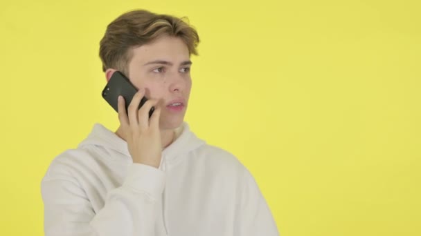 Молодой человек злится по телефону на желтом фоне — стоковое видео