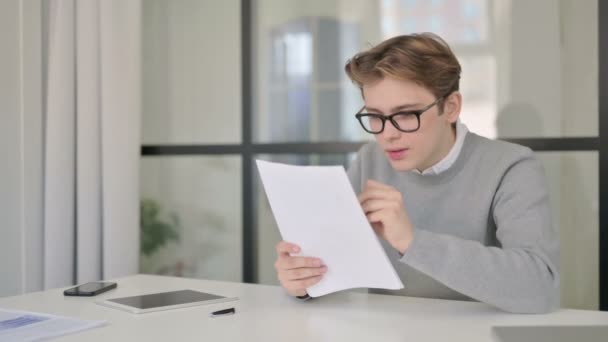 A fiatal férfi boldognak érzi magát, miközben dokumentumokat olvas a modern irodában — Stock videók