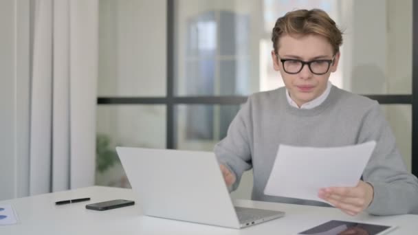 Jonge man met laptop leesdocumenten in modern kantoor — Stockvideo