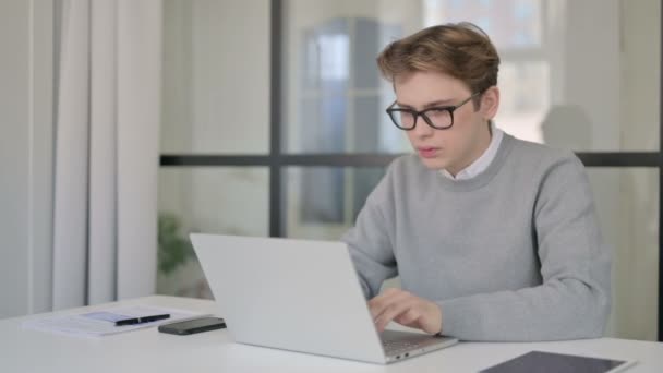 Hombre joven celebrando el éxito mientras usa el ordenador portátil en la oficina moderna — Vídeo de stock