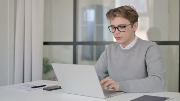 Ung man ler mot kameran när du använder laptop i moderna kontor — Stockvideo