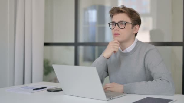 Junger Mann denkt beim Arbeiten am Laptop im modernen Büro — Stockvideo