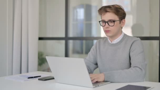 Hombre joven mostrando pulgares hacia arriba firmar mientras se utiliza el ordenador portátil en el trabajo — Vídeo de stock