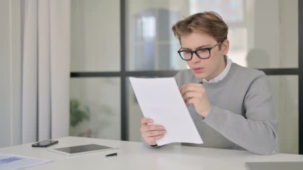 Молодой человек читает документы, сидя в современном офисе — стоковое видео