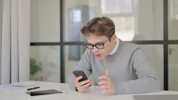 Sorglig ung man reagerar på förlust på Smartphone i Office — Stockvideo