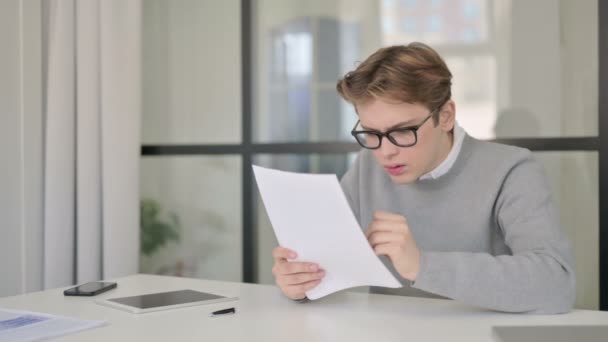 Молодой человек грустит, читая документы в современном офисе — стоковое видео