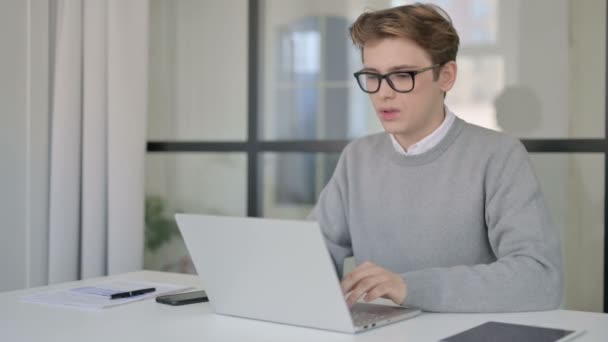 Hombre joven que tiene dolor de espalda mientras usa el ordenador portátil en la oficina moderna — Vídeos de Stock