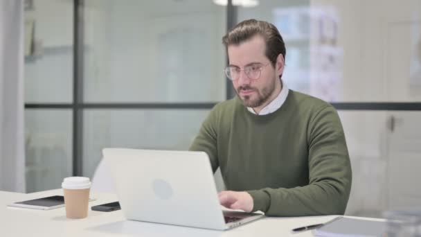 Junger Geschäftsmann zeigt Daumen hoch, während er Laptop im Büro benutzt — Stockvideo