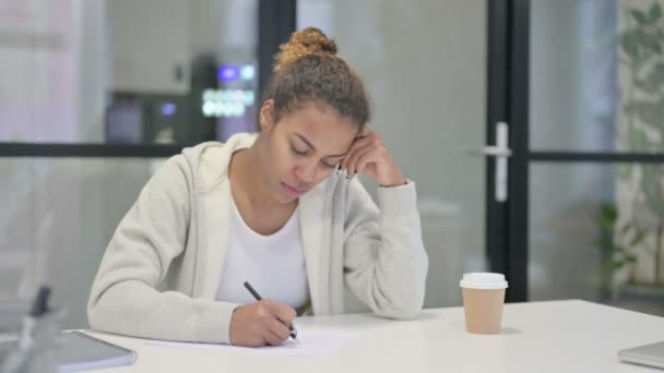 Αφρικανική γυναίκα σκέφτεται ενώ γράφει στο χαρτί στο γραφείο — Αρχείο Βίντεο