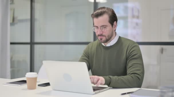 Joven Empresario sonriendo a la cámara mientras usa el ordenador portátil en la oficina — Vídeos de Stock