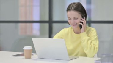 Ofiste dizüstü bilgisayar kullanırken Smartphone 'da Konuşan Genç Kadın