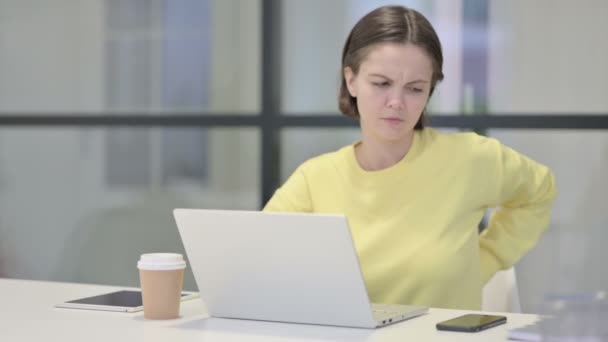 Молодая женщина с болями в спине во время использования ноутбука в офисе — стоковое видео