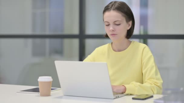 Junge Frau blickt im Büro mit Laptop auf Kamera — Stockvideo