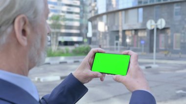 Yaşlı adam Krom Ekranlı Akıllı Telefona Bakıyor, Açık Hava