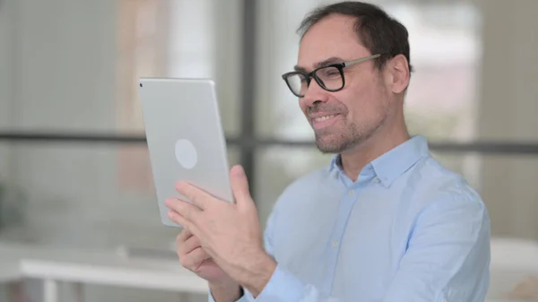 Видеозвонок на планшете от человека среднего возраста в офисе — стоковое фото