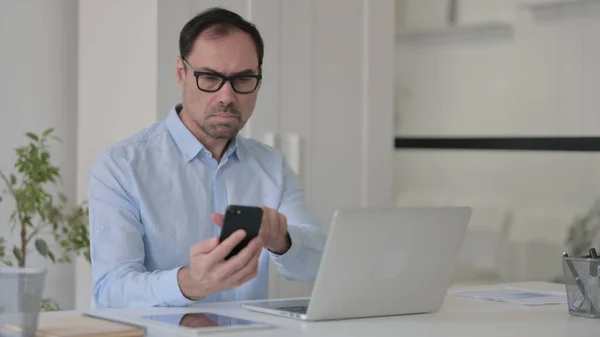 Uomo di mezza età utilizzando Smartphone mentre si lavora sul computer portatile — Foto Stock