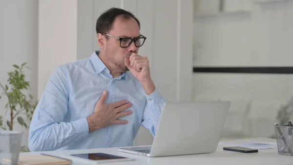 Mann mittleren Alters hustet, während er Laptop im Büro benutzt — Stockfoto