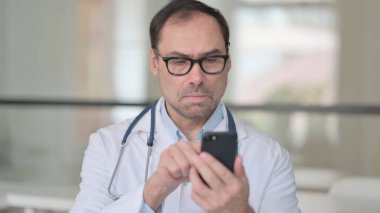 Orta yaşlı doktor akıllı telefon kullanıyor.