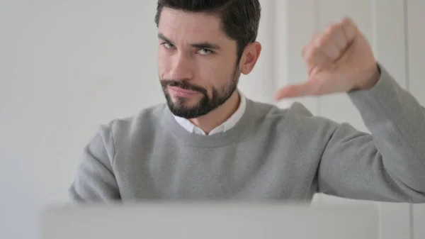 Primo piano di giovane uomo che mostra pollici giù durante l'utilizzo del computer portatile — Foto Stock