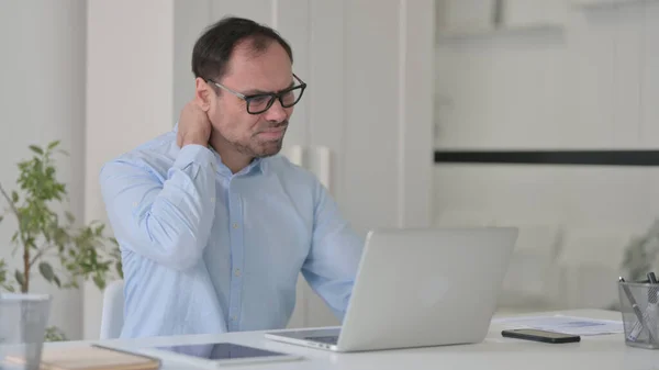 Dizüstü bilgisayarda yazarken boynu ağrıyan orta yaşlı bir adam — Stok fotoğraf