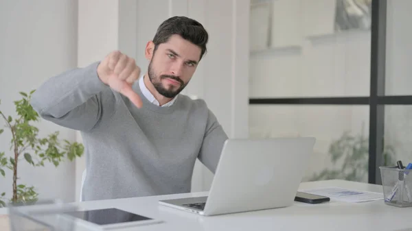Jeune homme montrant pouce vers le bas signe tout en utilisant un ordinateur portable au travail — Photo