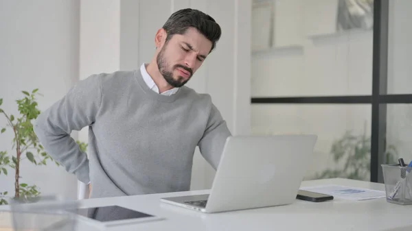 Junger Mann hat Rückenschmerzen, während er Laptop im Büro benutzt — Stockfoto