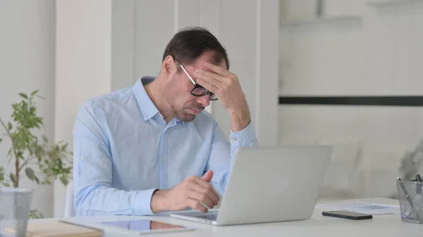 Homem de meia-idade com dor de cabeça trabalhando no laptop no escritório — Fotografia de Stock