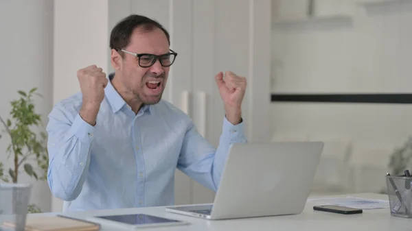 Hombre de mediana edad se siente sorprendido mientras se utiliza el ordenador portátil en la oficina — Foto de Stock