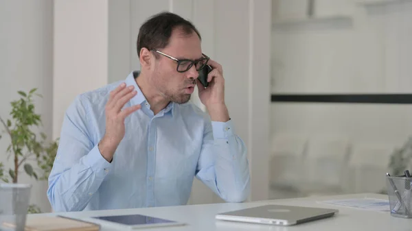 Wütender Mann mittleren Alters spricht im Büro auf Smartphone — Stockfoto
