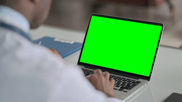 Vista trasera del médico africano utilizando el ordenador portátil con pantalla de croma verde —  Fotos de Stock
