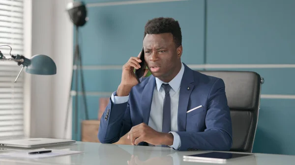 Naštvaný africký podnikatel mluví po telefonu v kanceláři — Stock fotografie