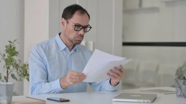 Mann mittleren Alters liest Dokumente im Büro — Stockfoto