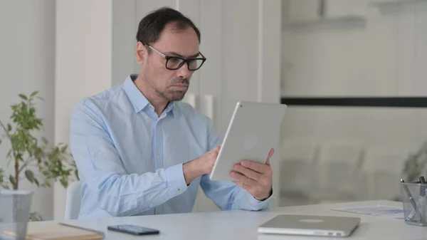 Привлекательный мужчина средних лет с помощью планшета в офисе — стоковое фото