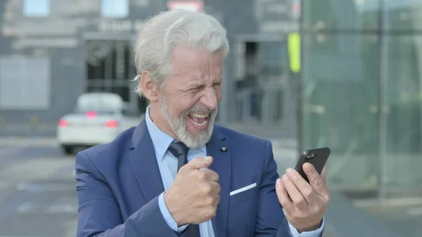 Viejo Empresario Celebrando en Smartphone mientras está parado al aire libre —  Fotos de Stock