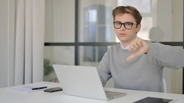 Junger Mann zeigt bei der Arbeit mit Laptop Daumen-runter-Zeichen — Stockfoto