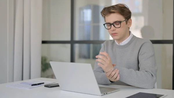 Hombre joven que tiene dolor de escritura mientras trabaja en el ordenador portátil en la oficina moderna — Foto de Stock