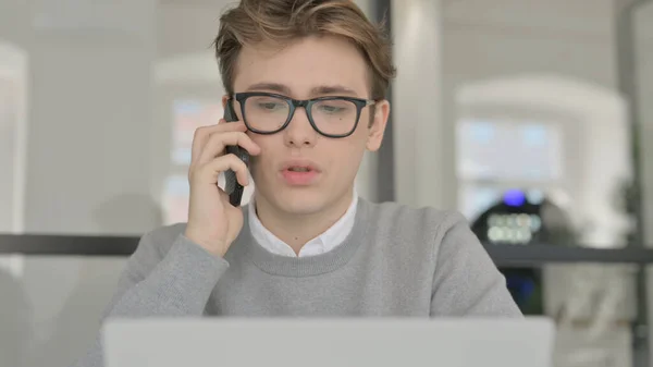 Primer plano del joven que habla por teléfono mientras trabaja en el ordenador portátil — Foto de Stock