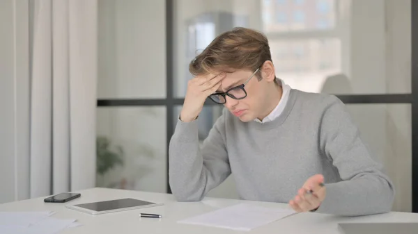 Junger Mann reagiert auf Verlust beim Schreiben auf Papier im Büro — Stockfoto