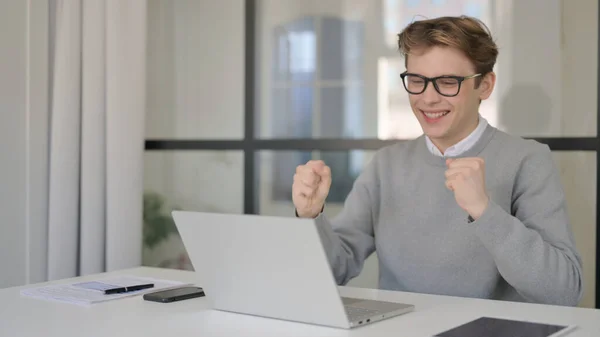 Hombre joven celebrando el éxito mientras usa el ordenador portátil en la oficina moderna — Foto de Stock