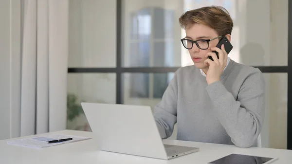 Jonge man praten op telefoon tijdens het gebruik van Laptop in Modern Office — Stockfoto