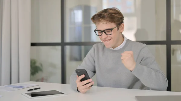 Attractive Young Man Celebrating Success on Smartphone in Office — Stock Photo, Image