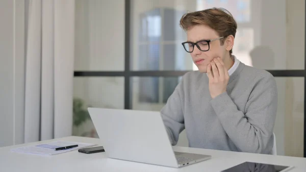 Jeune homme ayant mal aux dents tout en utilisant un ordinateur portable dans le bureau moderne — Photo