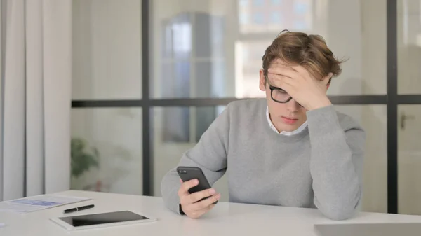 Junger Mann reagiert auf Verlust seines Smartphones im Büro — Stockfoto