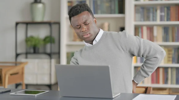 Homem Africano tendo dor nas costas ao usar laptop na biblioteca — Fotografia de Stock